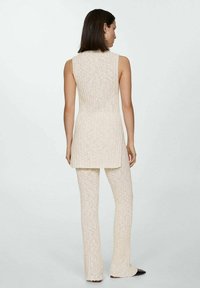 Beige stickad tvådelad outfit bestående av en ärmlös, ribbad tunika och matchande ribbade vida byxor med en mjuk textur och längande silhuett.