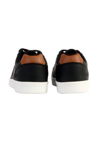Zapatillas negras con detalles en cuero marrón y suelas de goma blanca. Presentan un diseño elegante con material texturizado y un detalle de logo en la parte trasera.