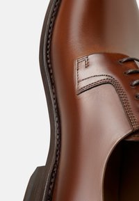 Braunes Leder Schuh mit glatter Textur, ausgestattet mit einer Schnürsenkeldesign, genähten Akzenten und einer gerundeten Zehenform. Minimalistische Ästhetik.