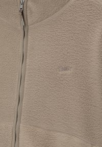 Veste polaire beige avec fermeture éclair complète, coutures visibles et petit logo brodé sur la poitrine.