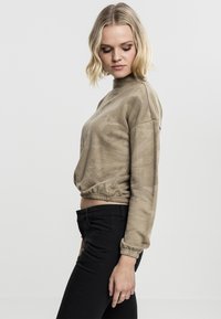Kuttet, lysebrun camouflagesweatshirt med høy hals, lange ermer og elastisk kant, paret med svarte tettsittende bukser.