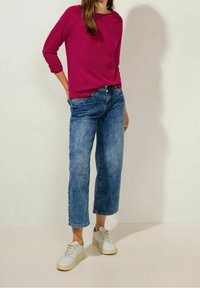 Fuchsiaram långärmad skjorta i kombination med ljusblå, korta denimjeans och vita sneakers. Slät tyg och avslappnad passform med subtila detaljer.