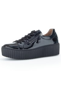 Schwarze Lackledersneaker mit schwarzen Schnürsenkeln, Reißverschlusdetail an der Seite und einer dicken, geriffelten Plattformsohle. Glatte Textur durchgehend.