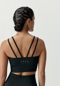 Svart sport-bh med flera ryggband, tillverkad av ett strukturerat tyg och med en figursydd design. Varumärkeslogotypen är placerad på ryggen.