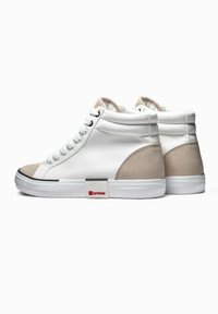 Zapatillas altas con parte superior de cuero blanco, detalles en ante beige, diseño texturizado y suela de goma con un logo rojo y plateado en el costado.