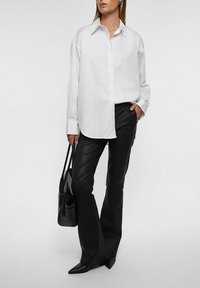 Valkoinen rento kauluspaita, yhdistetty mustiin leveälahkeisiin nahkahousuihin. Malli pitää kädessään mustaa olkalaukkua ja käyttää kärjestä kärkisiä mustia kenkiä.