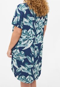 Kortärmad klänning i marinblått tyg med ett djärvt blommönster i nyanser av teal och vitt, med en avslappnad passform och rundad fåll.