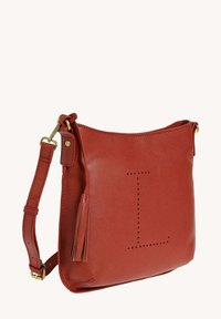Sac bandoulière en cuir rouge avec une texture, présentant une lettre "L" perforée bien visible et un accent de frange. Sangle ajustable incluse.