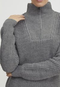 Grau gestrickter Pullover mit hohem Kragen und Reißverschluss. Verfügt über ein strukturiertes Muster und gerippte Bündchen für eine enge Passform.