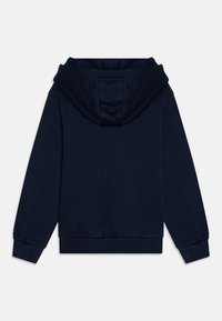 Tumši zila kapuce, kokvilnas materiāls, ar lielu kapuci un ribotām piedurknēm. Aizmugure ir vienkārša, bez logotipiem vai papildu detaļām.