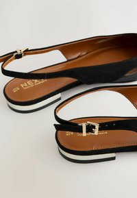 Sandales en cuir velours noir avec un bout ouvert, dotées d'une fine bride de cheville et d'une boucle en ton or. La semelle présente un détail de rayure blanche contrastante.