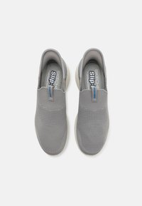 Scarpe slip-on grigie con tomaia in rete testurizzata, interno morbido e suola in gomma bianca a contrasto, con il marchio "SKECHERS" sulla linguetta.