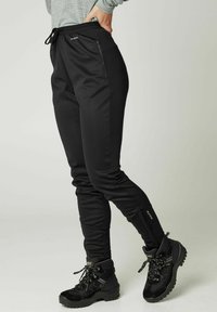 Zwarte sportieve broeken van rekbaar materiaal met een taps toelopende pasvorm, voorzien van ritszakken en een tailleband met trekkoord.