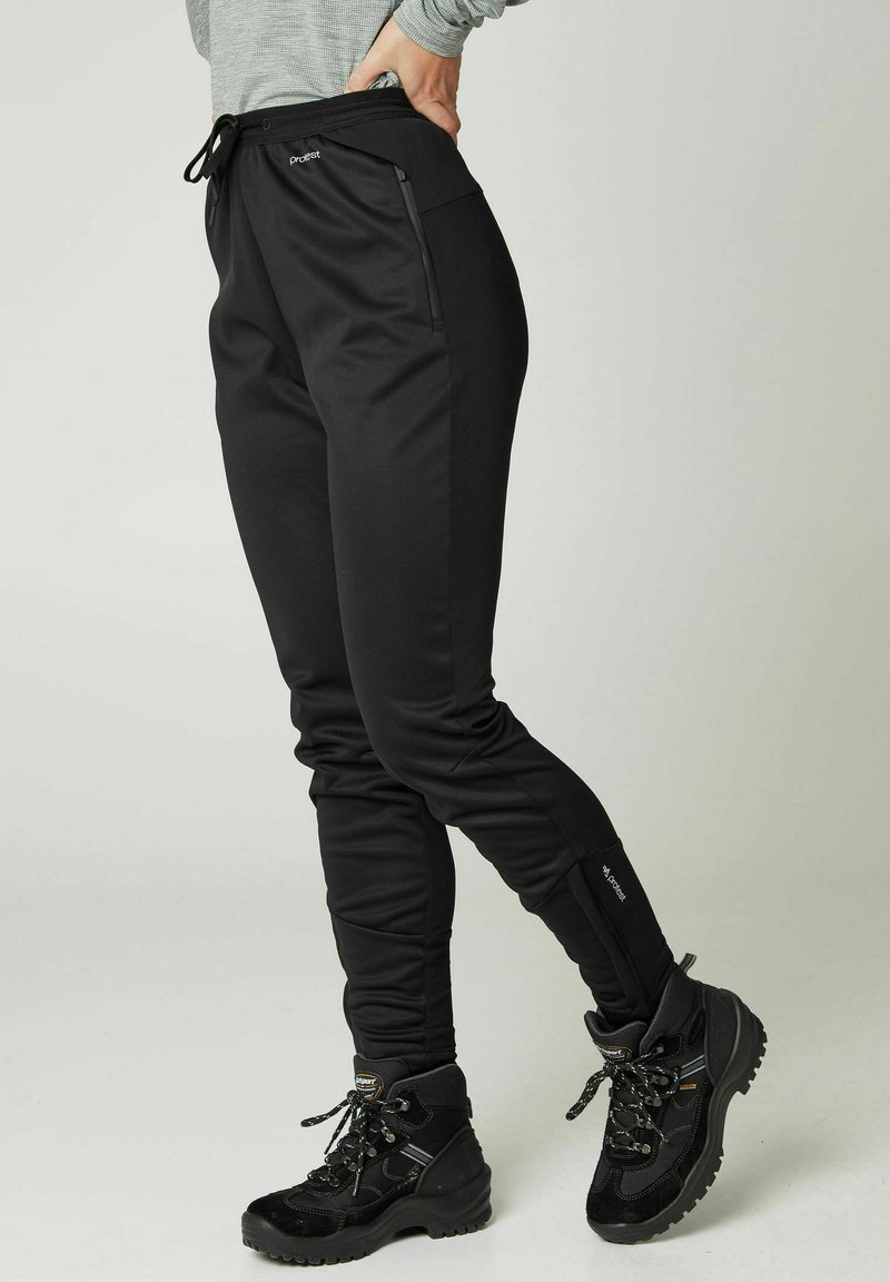 Zwarte sportieve broeken van rekbaar materiaal met een taps toelopende pasvorm, voorzien van ritszakken en een tailleband met trekkoord.