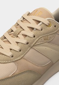 Μπεζ και ταμπά αθλητικό παπούτσι με μικτούς σουέντ και διχτυωτούς πίνακες, επίπεδα μπεζ κορδόνια, χρυσό ρεγκλόν και λογότυπο "GAP" στη γλώσσα και στο πλάι.