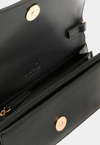 Borsa a tracolla in pelle nera con finitura testurizzata, dotata di un bottone a pressione circolare dorato e di un compartimento con zipper per una conservazione sicura.