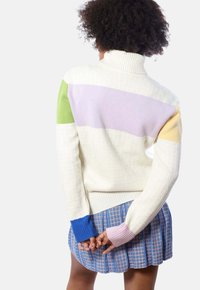 Cremfarbener, gerippter Pullover mit kräftigen horizontalen Streifen in Grün, Lavendel, Gelb und Blau. Kombiniert mit einem gefalteten blau karierten Rock.