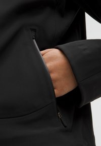 Musthave veekindel must jope, millel on tõmblukuga küljetasku ja sile, siidine tekstuur. Varrukad on kitsad ja üldine disain on minimalistlik.