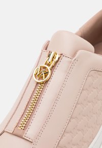Light pink sneaker featuring a gold zipper closure and circular logo accent. Textured surface with patterned details and contrasting stitching.