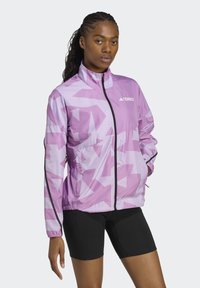 Lätt rosa jacka med geometriskt mönster, hel dragkedja och hög krage. Har svarta detaljer och elastiska manschetter för en snug passform.