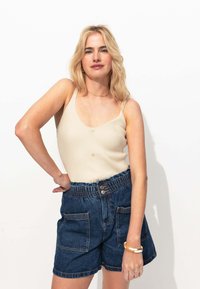 Débardeur beige côtelé avec des boutons, associé à un short en denim bleu avec une taille élastique et des poches avant, sur fond blanc.
