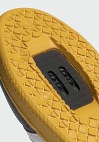 Semelle en caoutchouc jaune avec une surface texturée et à motifs, comportant une zone de clip noire pour se fixer aux pédales.