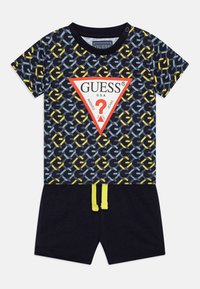 Mornarska odjeća kratkih rukava s geometrijskim uzorkom u plavoj, žutoj i bijeloj boji, s crvenim trokutastim logotipom i kratkim hlačama s žutom vezicom.