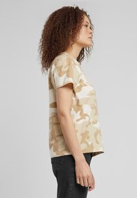 T-shirt con motivo camouflage in beige e crema, realizzata in cotone, con una vestibilità rilassata e maniche corte, caratterizzata da un design a collo rotondo.