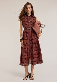 Red and patterned dress with a collar, sleeveless design, cinched waist, and flared skirt. Paired with a textured pink bag and black sandals.