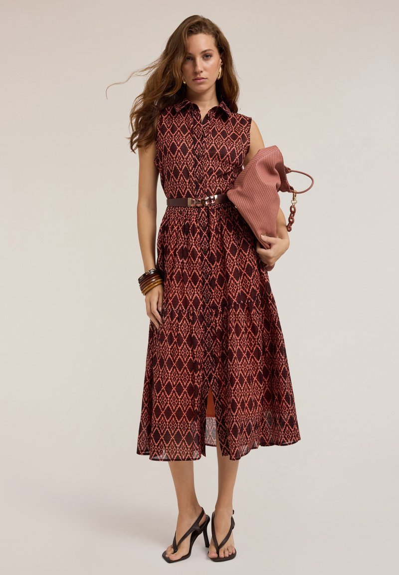 Red and patterned dress with a collar, sleeveless design, cinched waist, and flared skirt. Paired with a textured pink bag and black sandals.