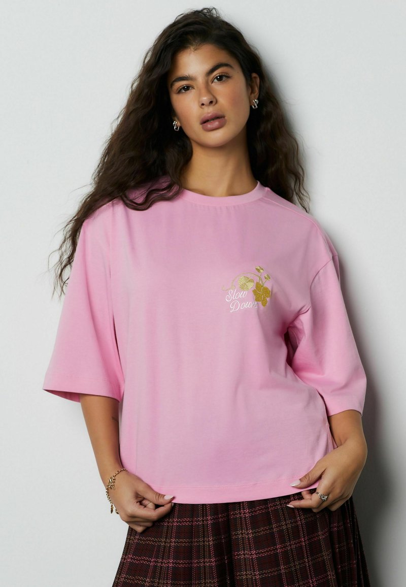 Pink kortærmet t-shirt lavet af bomuld med en afslappet pasform. Har teksten "Slow Down" og blomstermotiver i guld broderi.