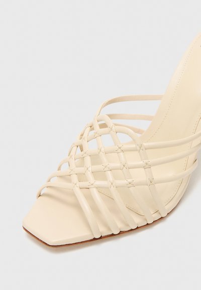 Sandalia beige con puntera abierta y frontal cuadrado, con tiras de cuero trenzado cruzando el pie, con un tacón de altura media.