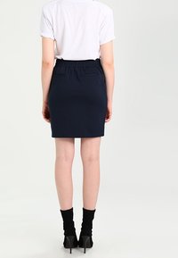 Marinblå blyertskjol med en figursydd design, elastisk midjeband, två bakfickor och en mjuk textur, kombinerad med svarta ankellånga strumpor och klackar.