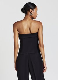 Schwarzes, trägerloses Oberteil mit strukturiertem Mieder, weitem Ausschnitt und glatter Textur, kombiniert mit maßgeschneiderten schwarzen Hosen.