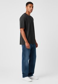 T-shirt nero a maniche corte abbinato a jeans blu e sneakers bianche. La maglietta ha una vestibilità comoda, una texture liscia e un design semplice.