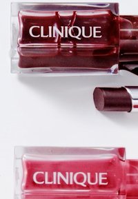 Två Clinique-läppprodukter i klart förpackning. Den ena är i en djup röd nyans, den andra i en stark rosa. Båda visar Clinique-logotypen tydligt.