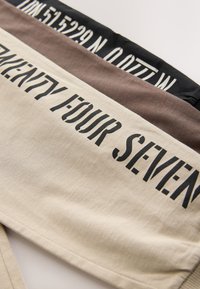 Katoenen stof in drie kleuren: beige, bruin en zwart. Elk heeft opvallende tekst: "TWENTY FOUR SEVEN" en coördinaten in contrasterend zwart.
