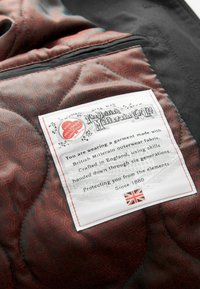 Tamsiai pilkas siuvinėjimas su subtiliu raudonu šešiakampiu raštu. Įtraukta balta etiketė, kuri detalizuoja amato meistriškumą, ir Didžiosios Britanijos vėliava.