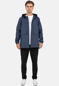 Marineblauwe lichtgewicht jas van waterafstotend materiaal, met een capuchon, twee voork_hexen, elastische manchetten en een rits over de volle lengte.