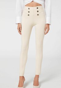 Leggings crème taille haute en tissu extensible. Présentent cinq boutons décoratifs et des coutures verticales sur l'avant.