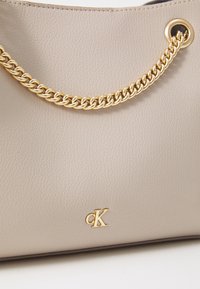 Borsa a mano in pelle grigio chiaro con tracolla a catena dorata, logo impresso in oro e texture liscia con forma strutturata.