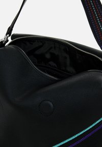 Sac en cuir noir avec une ouverture zippée. Présente des coutures colorées en turquoise, violet et rouge. Intérieur doublé en tissu noir.