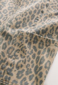 Gros plan d'un tissu beige avec imprimé léopard gris foncé et coutures visibles ainsi que surpiqûres de poche.