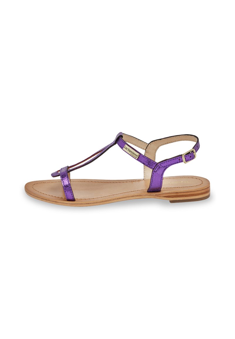 Sandale en métal violet avec un design à T, boucle ajustable à la cheville et semelle plate. Comprend une semelle intérieure nude et un léger talon en bois.