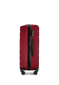 Maleta rígida roja con una superficie texturizada, cremalleras y asa negra, y cuatro ruedas multidireccionales para facilitar la maniobrabilidad.