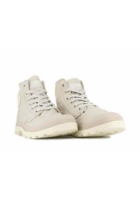 Scarpe alte beige chiaro in tela. Caratteristiche includono lacci piatti, suola texturizzata e una toppa rotonda con logo sul lato.