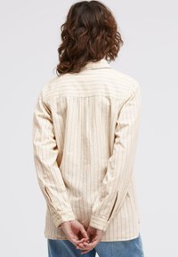 Cream-colored shirt with vertical stripes, buttoned cuff sleeves, and side slits. Soft fabric with a relaxed fit and classic collar.