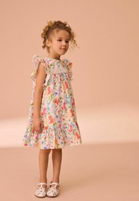 Bloemrijke jurk met gerimpelde mouwen, met een gathered lijfje en gelaagde zoom. Complementair met witte sandalen met bandjes.
