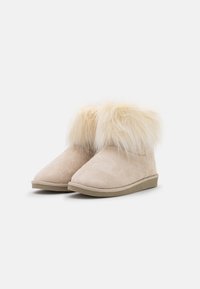 Beige Wildleder-Stiefeletten mit einem weichen, leichten Fellbesatz am oberen Rand, runder Zehenform und flacher Gummisohle.