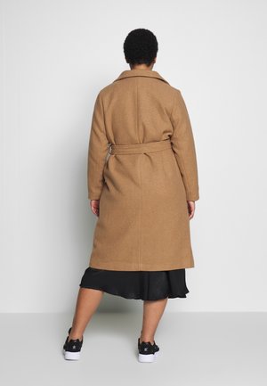 Manteau en mélange de laine brun avec une taille ceinturée, un col et une coupe mi-genoux, porté sur une robe noire et associé à des baskets noires.